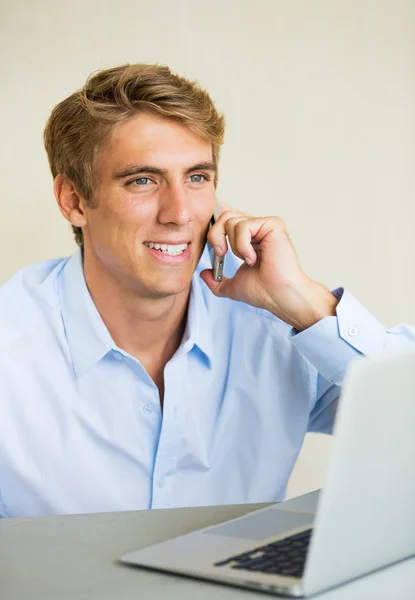 Jovem trabalhando no computador portátil conversando no telefone — Fotografia de Stock