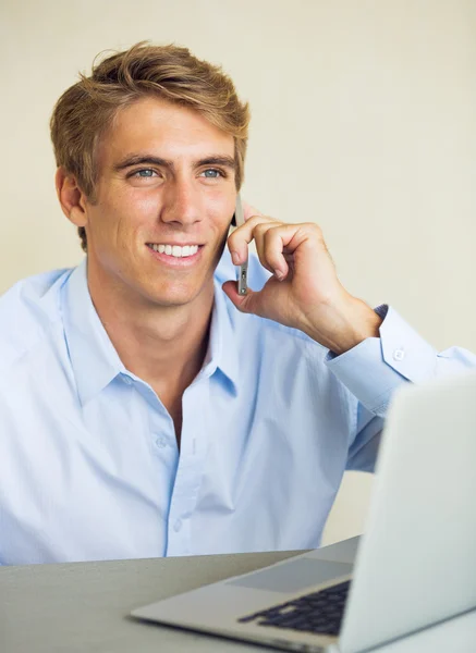 Jovem trabalhando no computador portátil conversando no telefone — Fotografia de Stock