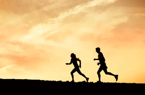 Man and woman runing together into sunset — Stock Photo, Image