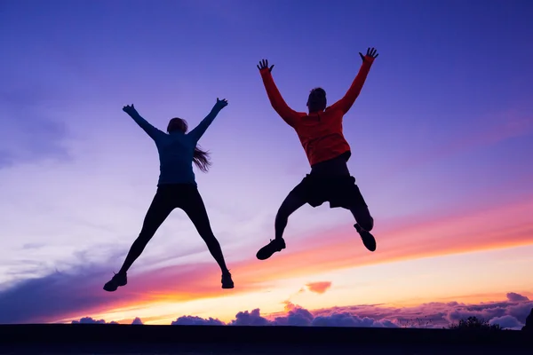 Gelukkig man en vrouw plezier springen in de lucht bij zonsondergang — Stockfoto