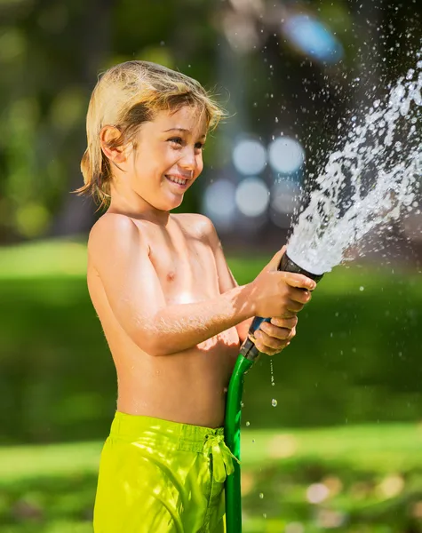 Kind, jongen of jongen speelt met waterslang buitenshuis — Stockfoto