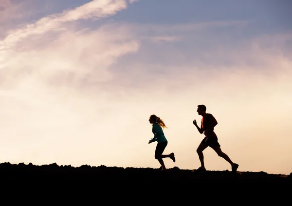 Silhouette of man and woman running jogging together into sunset — Stock Photo, Image