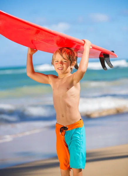 En lykkelig liten gutt på stranden med surfebrett. – stockfoto