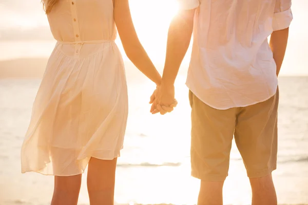 Um casal de mãos dadas ao pôr-do-sol na praia. Romântico jovem casal i — Fotografia de Stock