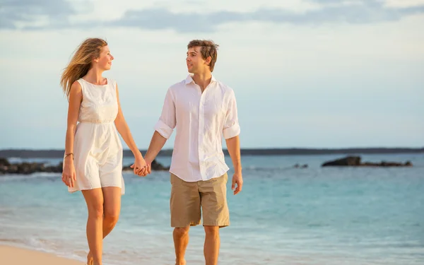 Romántica pareja feliz caminando en la playa al atardecer. Aguantamiento sonriente — Foto de Stock