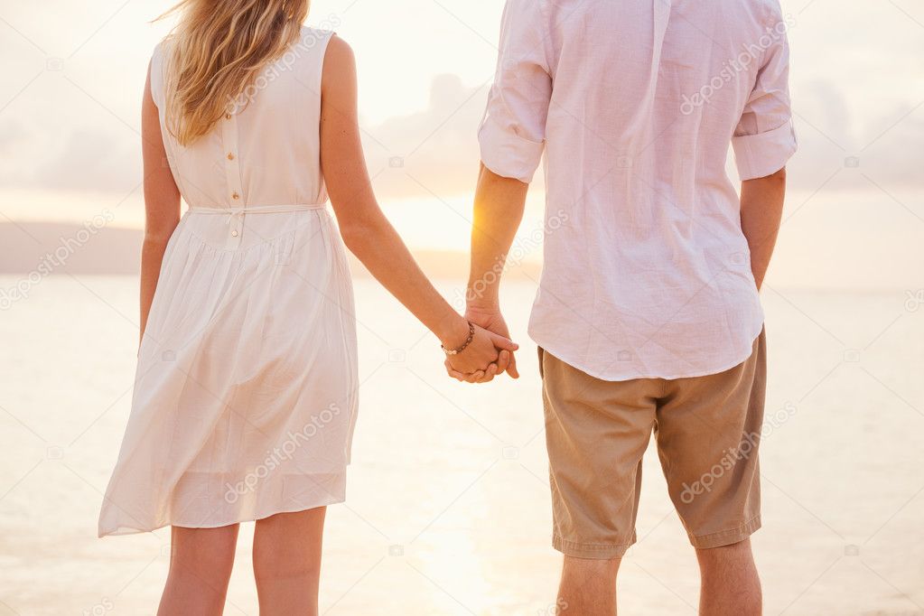 Couple holding hands at sunset on beach. Romantic young couple i