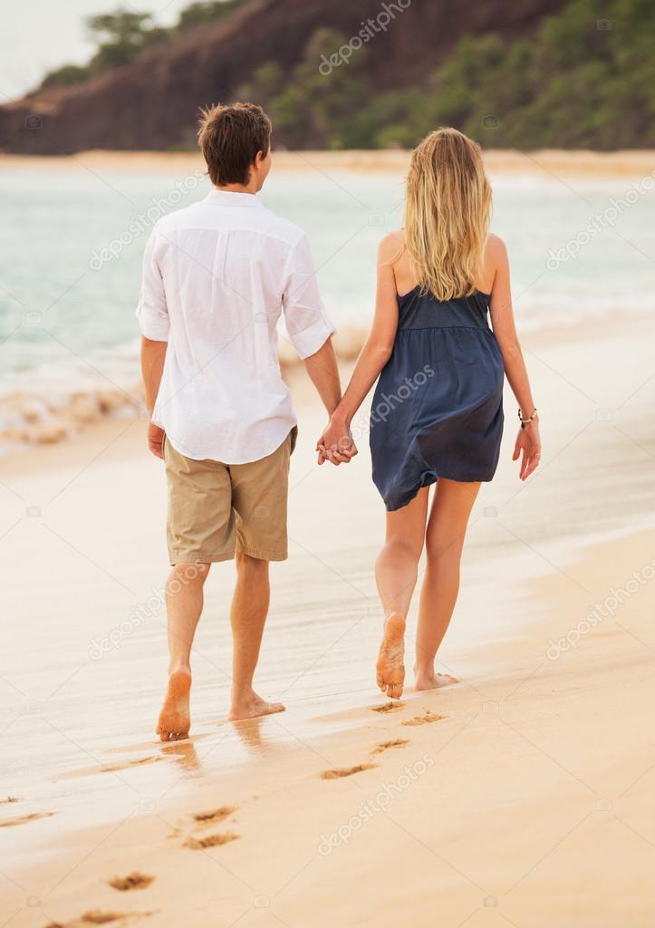 Romantic happy couple walking on beach at sunset. Smiling holdin