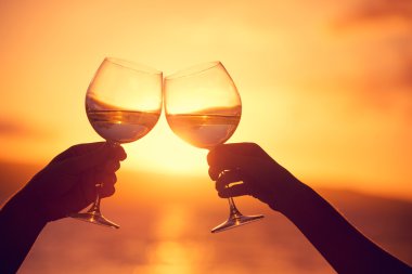 Man and woman clanging wine glasses with champagne at sunset dra