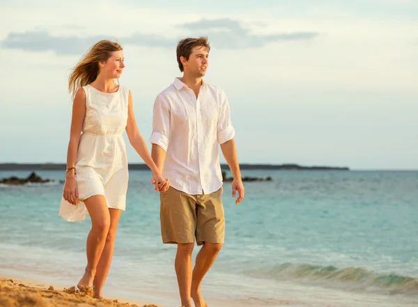 Pareja joven enamorada caminando por la playa al atardecer — Foto de Stock