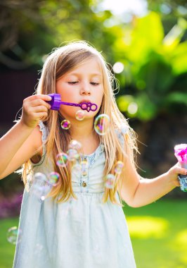 Tatlı küçük kız sabun köpüğü üflüyor.