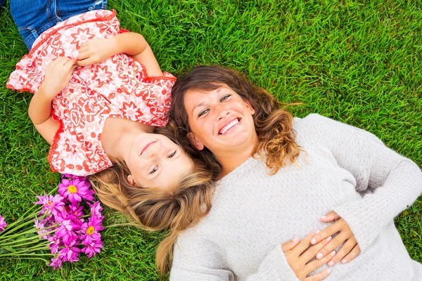 Glückliche Mutter und Tochter, die sich draußen auf grünem Gras entspannen. Ausgaben — Stockfoto