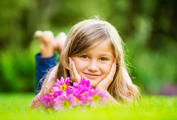 Yeşil çimenlerin üzerinde yatan gülümseyen küçük bir kızın portresi. — Stok fotoğraf