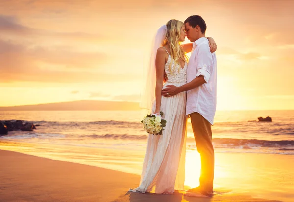 Braut und Bräutigam küssen sich bei Sonnenuntergang an einem wunderschönen tropischen Strand lizenzfreie Stockfotos