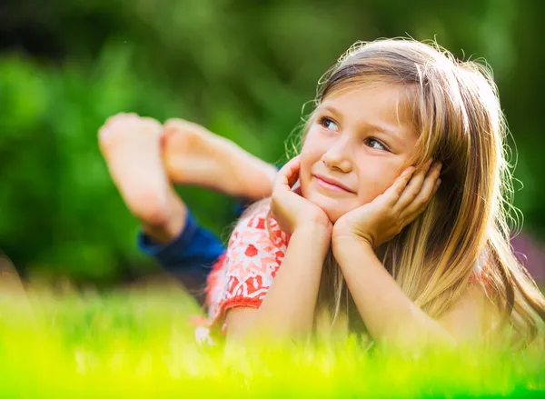 Portrait of a smiling little girl lying on green grass Royalty Free Stock Images