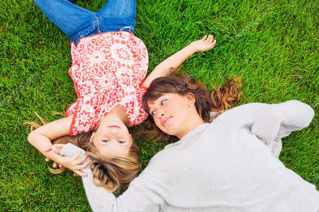 Happy mother and daughter relaxing outside on green grass. Spend