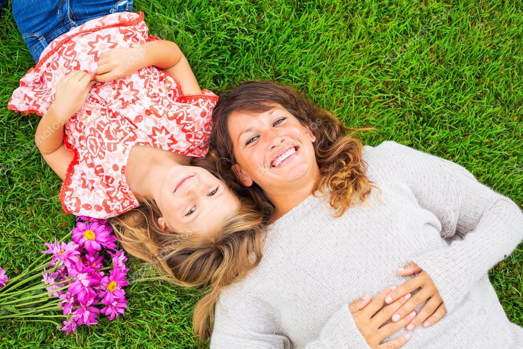 Happy mother and daughter relaxing outside on green grass. Spend