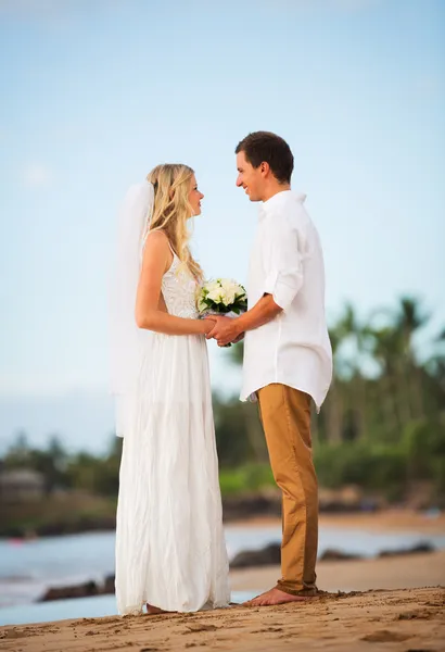 Просто женатая пара, держащаяся за руки на пляже на закате — стоковое фото