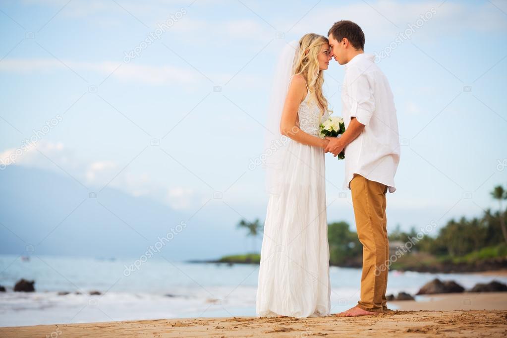 Just married couple holding hands on the beach at sunset