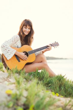 Güzel genç bir kadın sahilde gitar çalıyor.