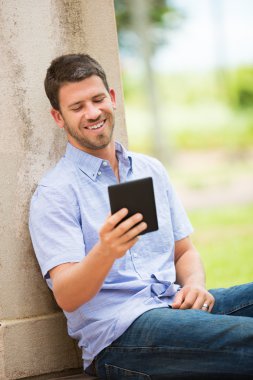 Young man reading E-book outside clipart