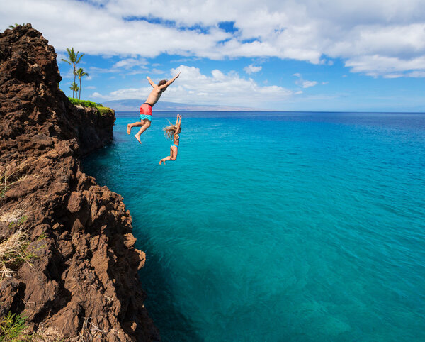 Friends cliff jumping into the ocean