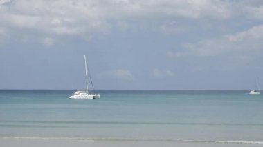 the beach with a few yachts in sea, white sand and wave from peaceful sea in sunshine daytime