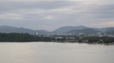 Phuket kasabası, arka planında dağ olan plaj koyunun yanında gün batımında deniz olan.