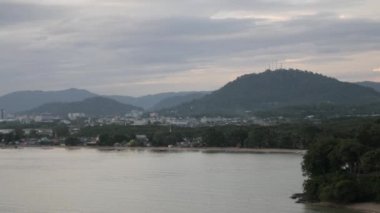 Phuket kasabası, arka planında dağ olan plaj koyunun yanında gün batımında deniz olan.