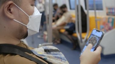 Asyalı adam toplu metro ulaşımı sırasında akıllı telefon kullanıyor.