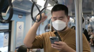 Asyalı adam trabzan tutarken akıllı telefon kullanıyor. Ya da metro ulaşımında kayışları tutuyor.