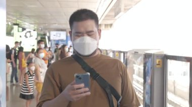 Bangkok 'ta metro toplu taşıma trenini beklerken cep telefonu çalan maskeli bir adam.