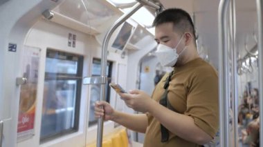 Asyalı adam metro ulaşımında akıllı telefon kullanıyor.