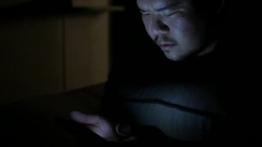 Asyalı adam cep telefonuyla sohbet ederken ve gece vakti yatakta uzanırken.
