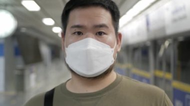 Bangkok 'ta metroyu beklerken maske takan bir adam gülümsüyor.
