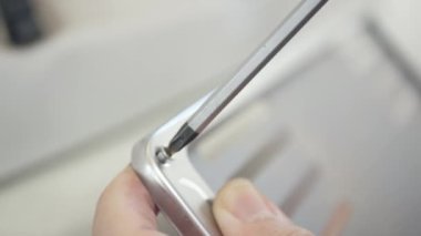 Manzara teknisyeni arabanın plakasındaki tornavidayla vidayı söküyor. Adamın biri vidayı sökmek için tornavida kullanıyor.