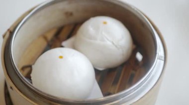 hand while picking chinese cream bun dimsum from basket steamer in chinese restaurant