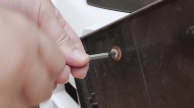 close up view mechanician unscrews the screw with a screwdriver from car's license plate. A man uses a screwdriver to unscrew a screw