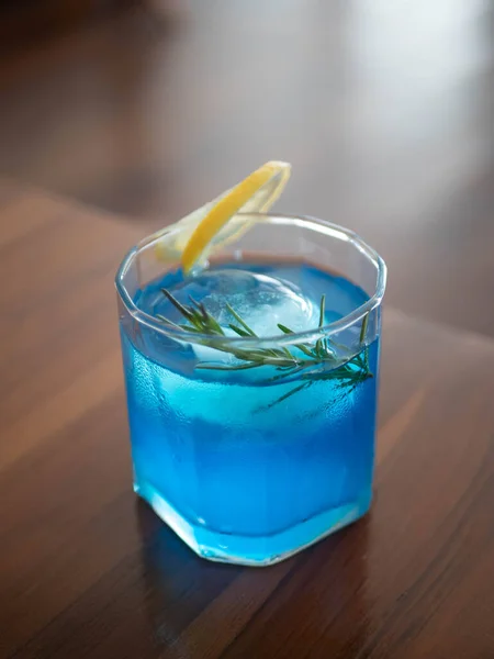 fresh ice blue liquor cocktail alcohol drink with lemon and rosemary in beautiful glass
