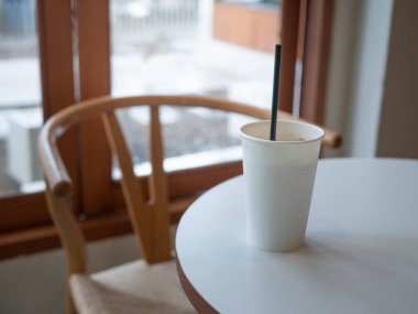 ice milk coffee in white plain empty paper cup on table near glass window in minimal japanese style cafe