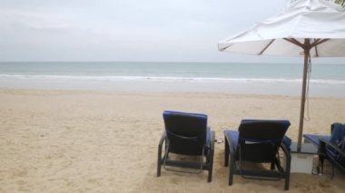 Tayland 'da beyaz kumsalda şemsiyeli lüks plaj yatakları güneşli yaz havası ve açık mavi gökyüzü.