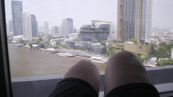 タイのバンコクにあるChaophraya川を望むリビングルームの大きな窓の近くのソファでリラックスしながら人の足にビュー — ストック動画