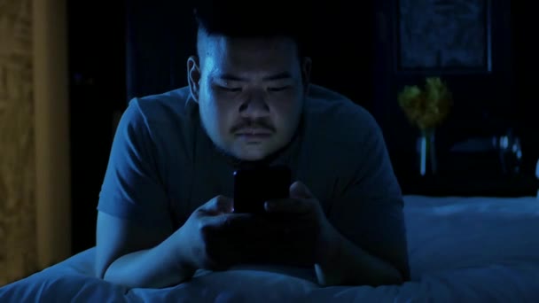 아시아인 남자가 침대에서 긴장을 침대에 누워서 스마트폰을 사용하고 있습니다 — 비디오