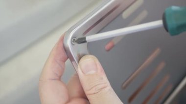 Manzara teknisyeni arabanın plakasındaki tornavidayla vidayı söküyor. Adamın biri vidayı sökmek için tornavida kullanıyor.