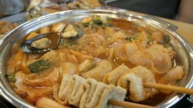 close up while using chopstick pick squid from Korean Kimchi tteok pokki soup with mussels, fish Ehmook, seafood and vegetable. Asain korean traditional food