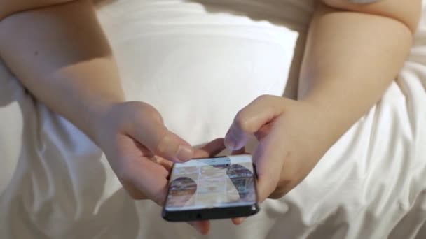 아시아인 남자가 침대에서 긴장을 침대에 누워서 스마트폰을 사용하고 있습니다 — 비디오
