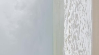 Yazın dalgalı deniz manzaralı dikey görüntü. Mavi gökyüzü ve beyaz bulutlu güzel tropikal plaj. Yaz tatili ve doğa çevresi plaj alanı kavramı.