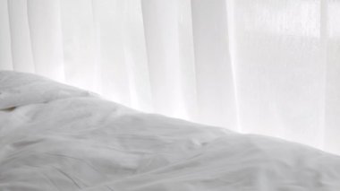 Beyaz perdeli, penceresinden güneş ışığı geçen beyaz perdeli, bembeyaz keten çarşaflı, rahat yatak odasında sabahın erken saatlerinde, arka planda doğal olarak.