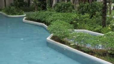 Modern tasarım merkezindeki tropikal ağaçlarla dolu ılık, rahatlatıcı yüzme havuzunun manzarası kasvetli hava zamanıyla