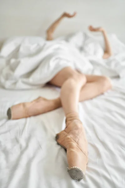 Woman in pointe shoes shows her legs and arms from under coverlet — Stock Photo, Image