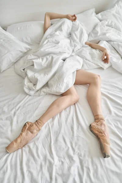 Женщина в пуантах показывает свои ноги и руки из-под одеяла — стоковое фото